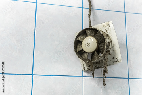 Close-up view of a heavily soiled and dusty exhaust fan mounted on a tiled wall, emphasizing the urgent need for thorough cleaning and regular maintenance to ensure proper hygiene. Housework