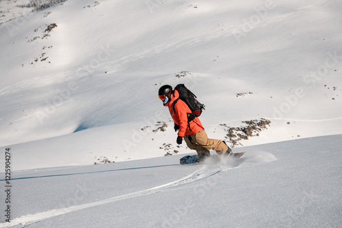 Extreme splitboarder in a helmet and goggles makes a descent on his splitboard on a snowy mountain slope photo