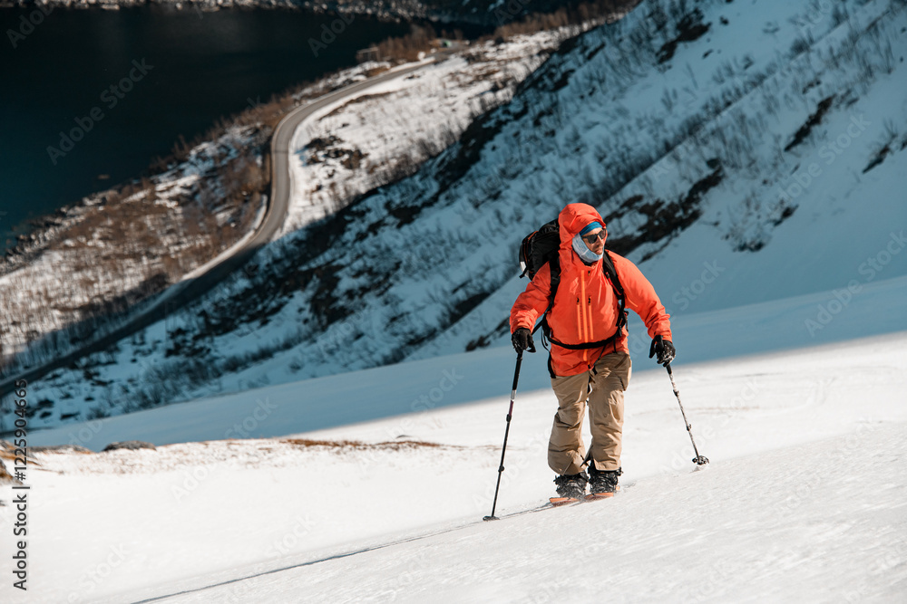 Skier in an orange jacket is skiing up the mountain, looking around Skier in an orange jacket is skiing up the mountain, looking around