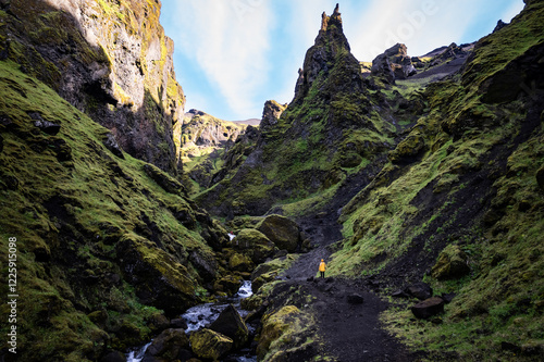 A woman in yellow jacket exploring and hiking a scenic mountain canyon with green vegetation near Thakgil (Pakgil) campsite in Iceland