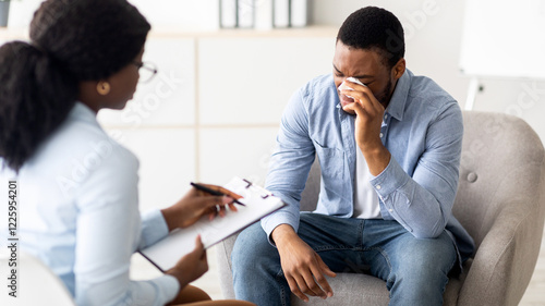Fotografija Depressed black guy crying at psychotherapist's office, seeking professional help at clinic