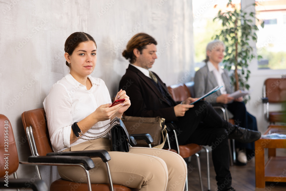 Interested young girl reading about potential employer on internet on phone while waiting for job interview sitting in office lobby Interested young girl reading about potential employer on internet on phone while waiting for job interview sitting in office lobby