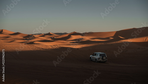 Fototapeta Naklejka Na Ścianę i Meble -  Off road vehicle stands amidst the undulating sand dunes of erg chebbi in merzouga desert, morocco, bathed in the warm glow of the setting sun