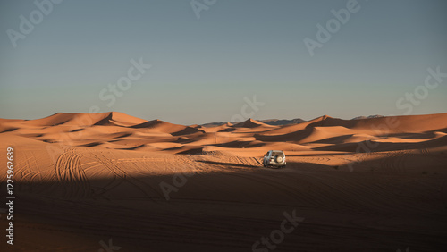 White off road vehicle navigating the mesmerizing erg chebbi dunes in merzouga desert, morocco, under the vast expanse of the late afternoon sky