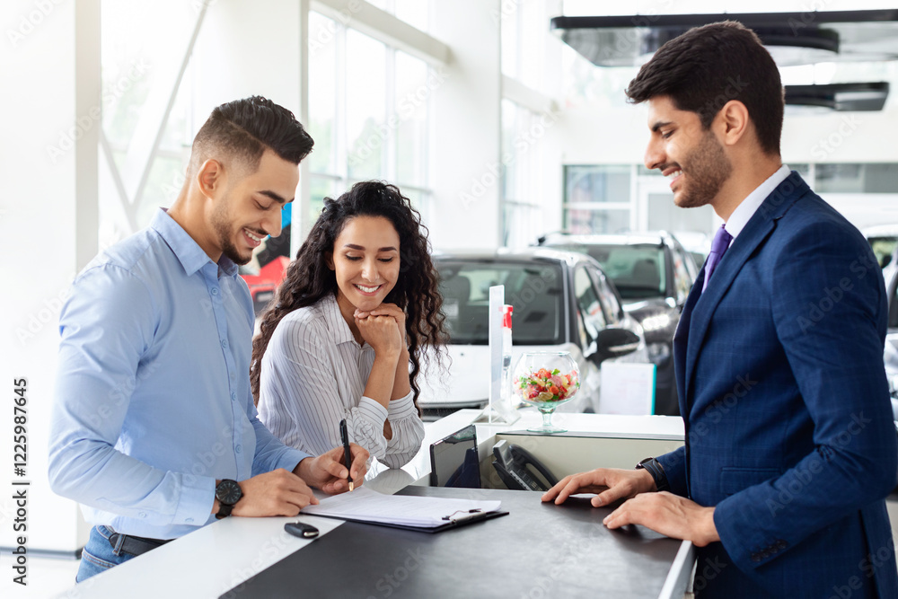 Wealthy arab family buying new car in showroom, standing by counter with handsome man sales assistant in suit, filling papers and having conversation. Car retail, leasing, auto showroom, salon concept Wealthy arab family buying new car in showroom, standing by counter with handsome man sales assistant in suit, filling papers and having conversation. Car retail, leasing, auto showroom, salon concept