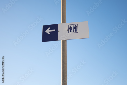 Restroom direction sign against clear blue sky photo