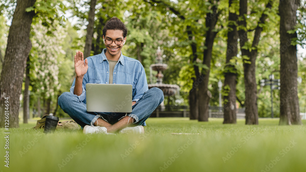 Young mixed-race student businessman talking having video call conversation online on laptop, vlogging blogging, watching webinar, lesson outdoors in city park on green grass lawn Young mixed-race student businessman talking having video call conversation online on laptop, vlogging blogging, watching webinar, lesson outdoors in city park on green grass lawn