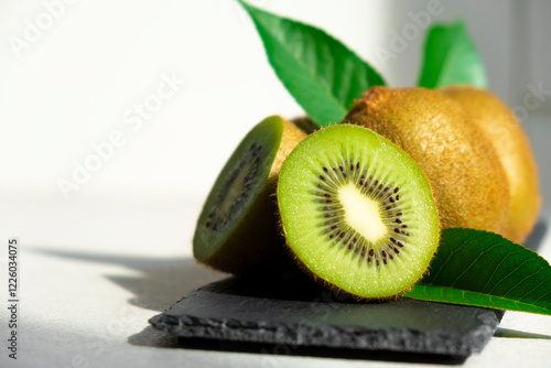 Ripe kiwi fruits in sunlight. Heap of whole kiwi fruits with green leaves and fresh cut kiwi on slate board. Healthy organic fruits full of vitamins and antioxidants. Green diet.