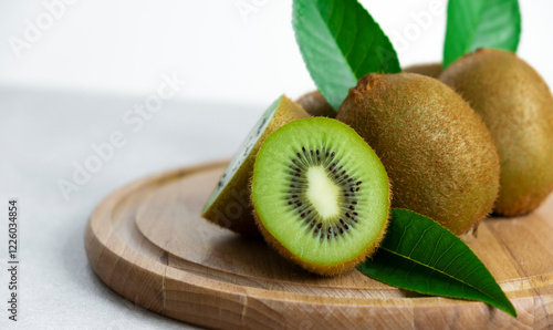 Ripe kiwi fruits in sunlight. Heap of whole kiwi fruits with green leaves and fresh cut kiwi on wooden cutting board. Healthy organic fruits full of vitamins and antioxidants.