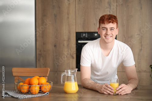 Young redhead man with glass of orange juice in kitchen