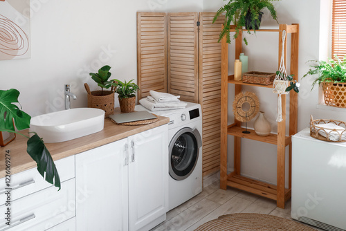 Interior of stylish laundry room with washing machine, sink and laptop on counter photo