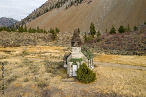 Abandoned church nestled in a mountain valley. Dried grasses and hills surround the weathered structure. St. Aidans Of Pokhaist Church, Pemynoos, British Columbia, Canada photo