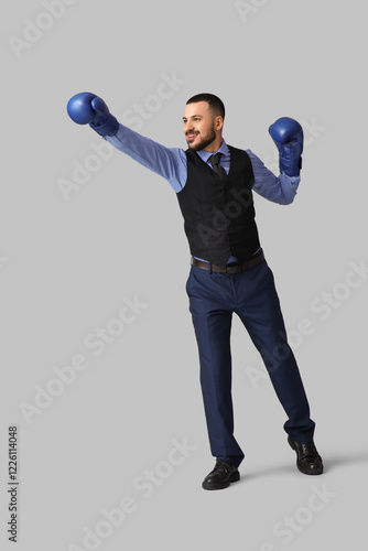 Young businessman in boxing gloves on grey background. Knockout concept