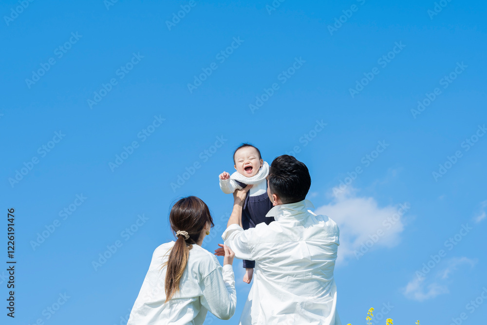 青空のもと、赤ちゃんを高く抱き上げる父母
