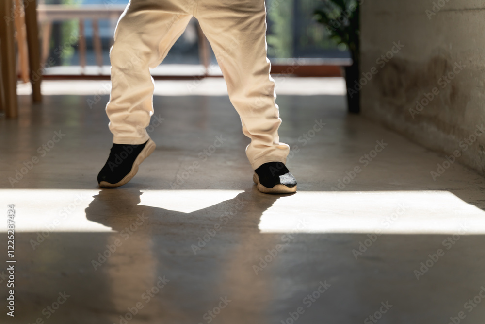 A child in beige pants and black sneakers standing indoors with sunlight casting shadows on the floor. A child in beige pants and black sneakers standing indoors with sunlight casting shadows on the floor.