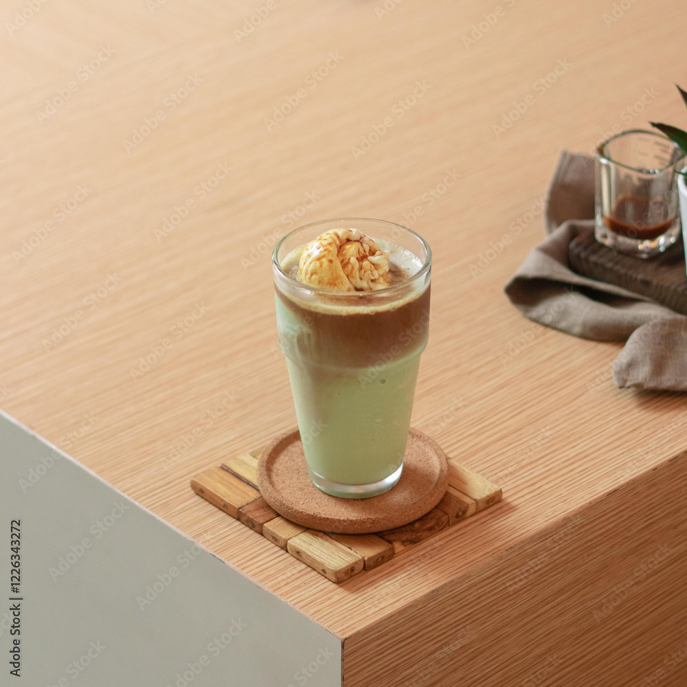 A delightful green tea beverage with creamy ice cream rests on a wooden table in a warm cafe, surrounded by a casual atmosphere A delightful green tea beverage with creamy ice cream rests on a wooden table in a warm cafe, surrounded by a casual atmosphere