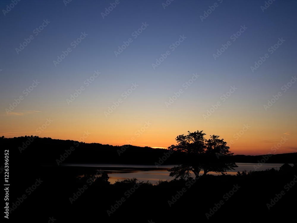 Obraz premium Sun setting over serene lake, with the warm glow of the fading light reflecting on the water and framed by a silhouette of a tree on the middle right side, serene, relaxing, scenic