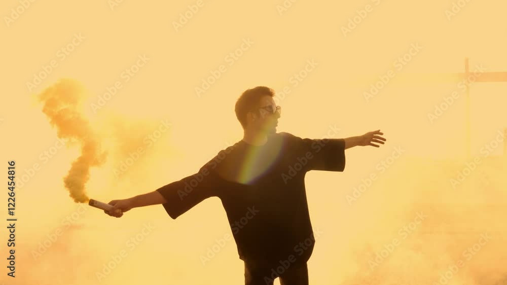 Handsome Young Man Hipster in Sunglasses Holding Smoke Bomb with Yellow Fume Standing on Rooftop at Sunset in the City Background 4K UHD B-Roll footage Handsome Young Man Hipster in Sunglasses Holding Smoke Bomb with Yellow Fume Standing on Rooftop at Sunset in the City Background 4K UHD B-Roll footage