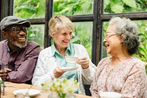 Принти на полотні Three diverse elderly friends enjoying tea and laughter at the table
