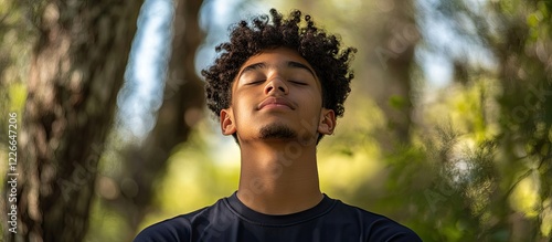 Teenage boy with curly hair meditating outdoors in natural green setting with soft sunlight highlighting his face promoting youth wellness and mindfulness