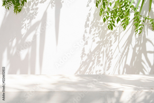 White table top with green leaves light and shadow on stucco wall texture background