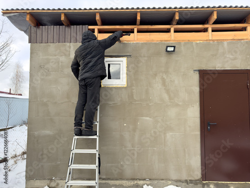 A man is on a ladder, painting a window photo