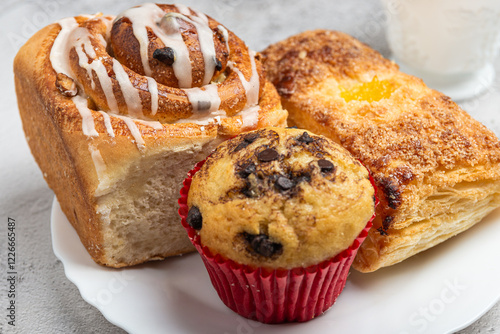 Close-up of a white plate with different freshly baked desserts, cinnamon roll, cupcake, and a sweet pastry. photo