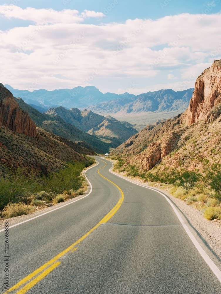 Fototapeta premium A long, curvy road winds through a desert landscape. The road is lined with trees and the mountains in the background create a sense of depth and vastness. The yellow lines on the road guide drivers