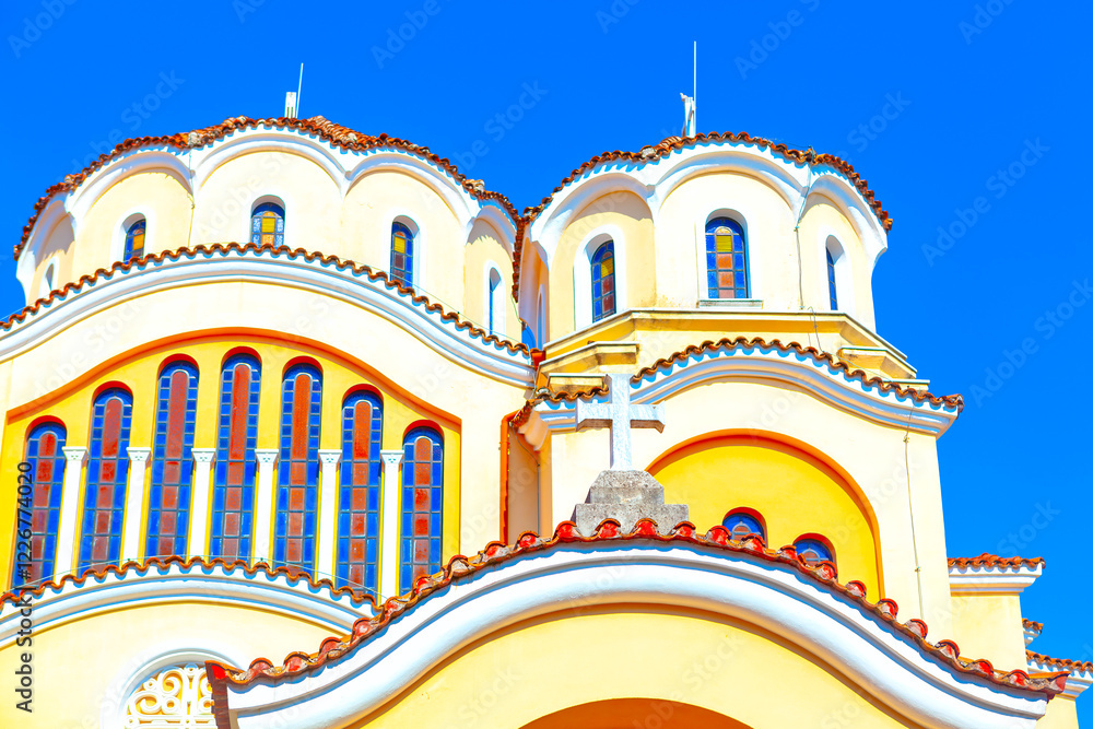 Domes of Shkoder Orthodox Cathedral in Albania. View of a beautiful yellow and white church with multiple domes, arched windows, and a cross on the roof, all set against a clear blue sky