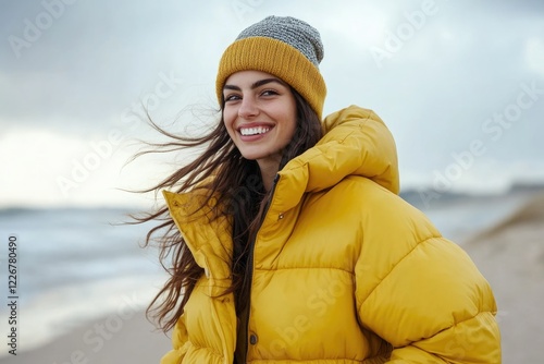 A woman wearing a yellow jacket and hat walks along the beach