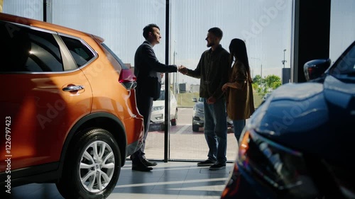 A young married couple receives the keys to a new car from the hands of a manager. Buying a family car