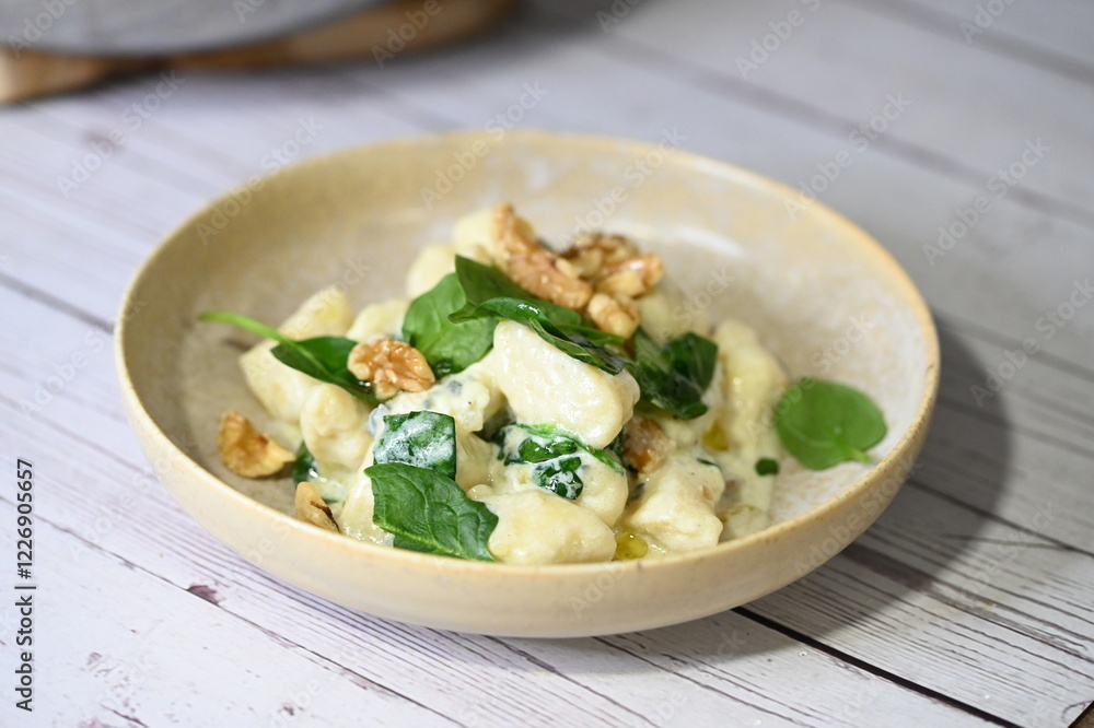 Close-up view of homemade potato gnocchi being prepared in the kitchen, with a creamy cheese sauce and fresh spinach leaves being added. Close-up view of homemade potato gnocchi being prepared in the kitchen, with a creamy cheese sauce and fresh spinach leaves being added.