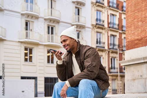 Young man sending a vocal message on his smartphone while sitting in the city