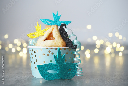 A beautifully dessert features a sweet Hamantaschen pastry in a decorative cup. The setup includes colorful masks and ribbon accents. Happy Purim carnival decoration photo