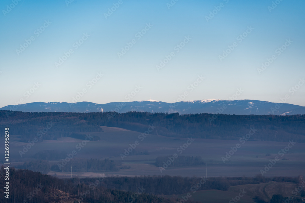 Distant view of the Jeseniky Mountains with Praded peak rising above the horizon. The vast landscape showcases rolling hills, deep forests, and the beauty of Czech nature