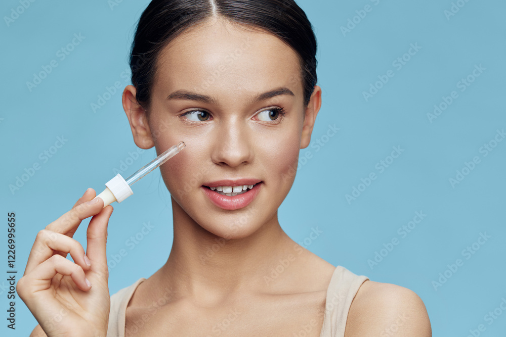 Young girl with light skin holding a skincare serum, smiling against a blue background, embodying a fresh and vibrant skincare routine Young girl with light skin holding a skincare serum, smiling against a blue background, embodying a fresh and vibrant skincare routine