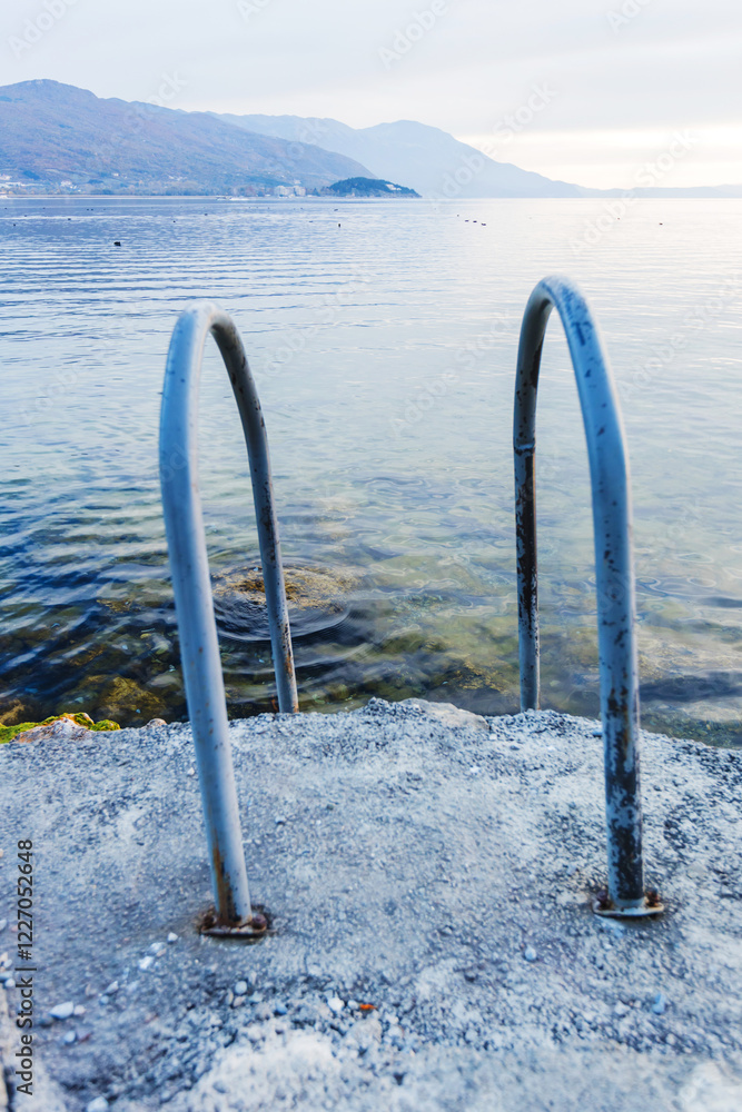 Fototapeta premium Serene Lakeside View with Ladder Leading into Clear, Calm Waters under a Mountainous Background