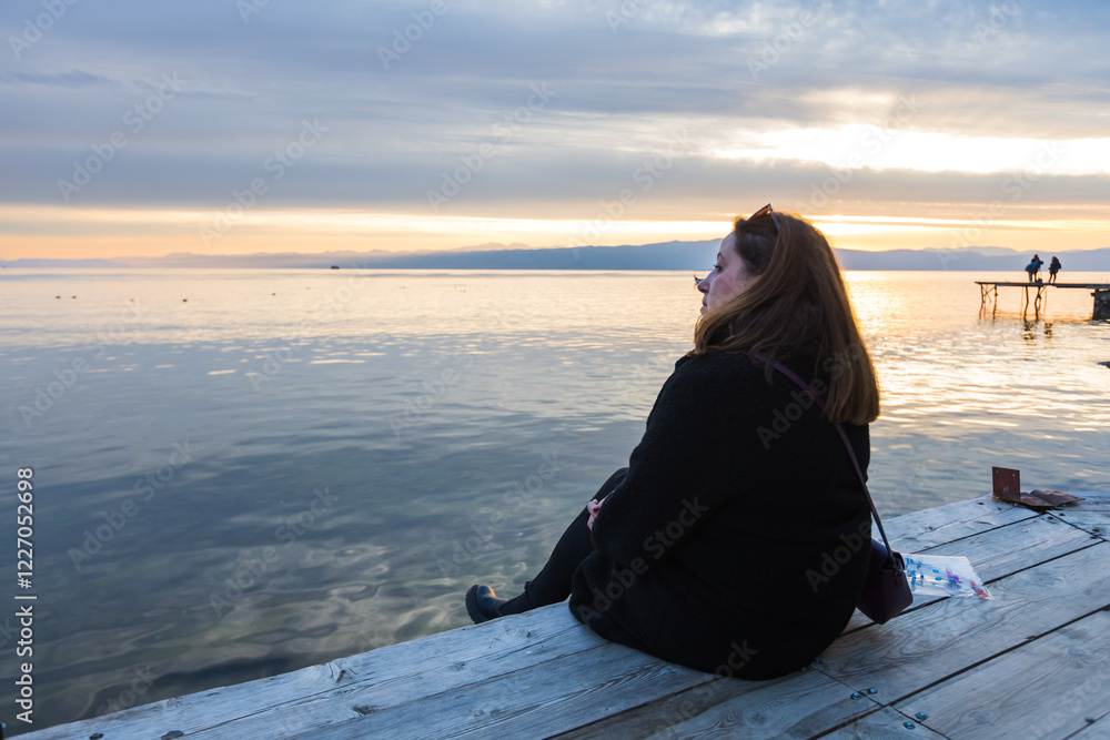 Peaceful moment as a woman enjoys the serene lake view and sunset, evoking calm and reflection. Peaceful moment as a woman enjoys the serene lake view and sunset, evoking calm and reflection.