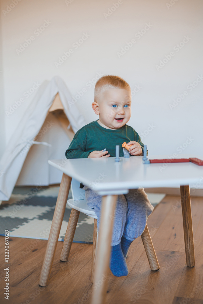 Blond boy toddler playing with toys in children's room close-up and copy space. Child sitting on a stool at a table. Furniture for children Blond boy toddler playing with toys in children's room close-up and copy space. Child sitting on a stool at a table. Furniture for children