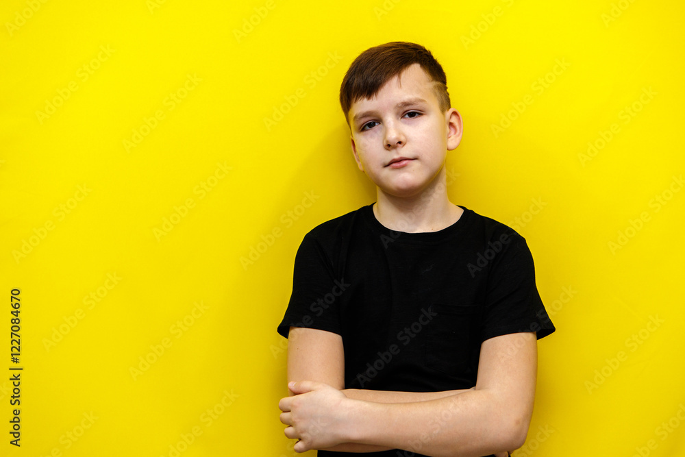 boy ten years old looking at camera with arms crossed on chest. portrait in black t-shirt on yellow background boy ten years old looking at camera with arms crossed on chest. portrait in black t-shirt on yellow background