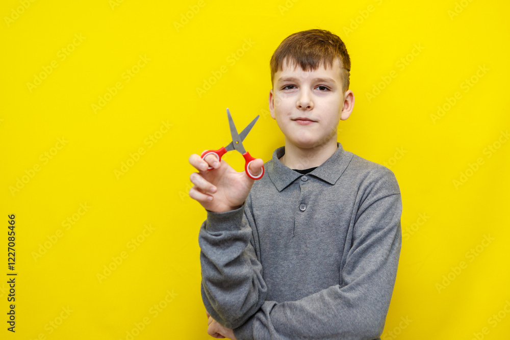 boy in gray sweater holds scissors in hand on yellow background boy in gray sweater holds scissors in hand on yellow background
