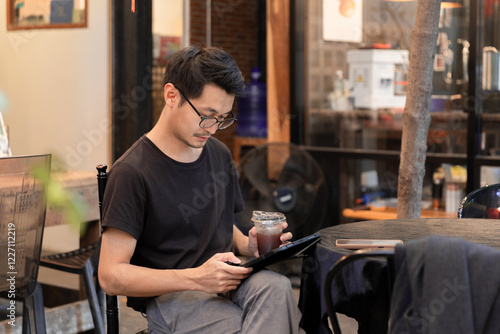 Young smiling freelancer typing message and drinking coffee