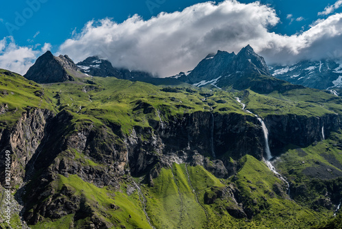 Witness the breathtaking beauty of the French Alps with this stunning photograph taken in Savoie. The image captures a dramatic mountainous landscape featuring lush green slopes and rugged rocky cliff