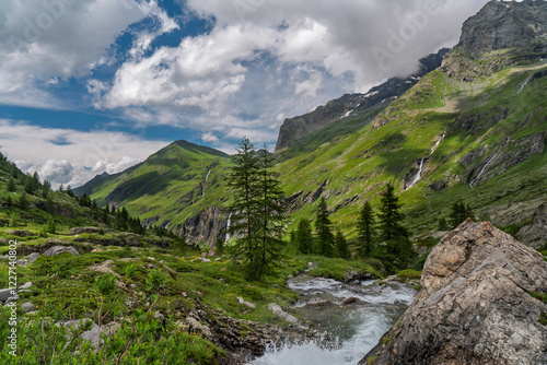 Witness the breathtaking beauty of the French Alps with this stunning photograph taken in Savoie. The image captures a dramatic mountainous landscape featuring lush green slopes and rugged rocky cliff
