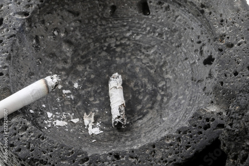 Lit cigarette and ash in black ashtray of volcanic stone. photo