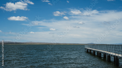 Wallpaper Mural A long wooden dock extends into a calm lake on a sunny day. The water is a deep blue-green color and there are ripples on the surface. The sky is clear with a few white clouds. Torontodigital.ca