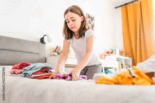Cute little girl sorting clothes in her room. Child folds messy stack of clothes. Home chores concept.