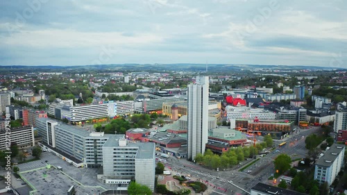 Aerial footage of Chemnitz Stadthalle surrounded by tall buildings under a cloudy sky, showcasing urban architecture and city dynamics. Drone move forward