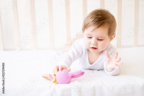 a small child close-up on a white cotton bed at home with a pink rodent, the baby is teething photo