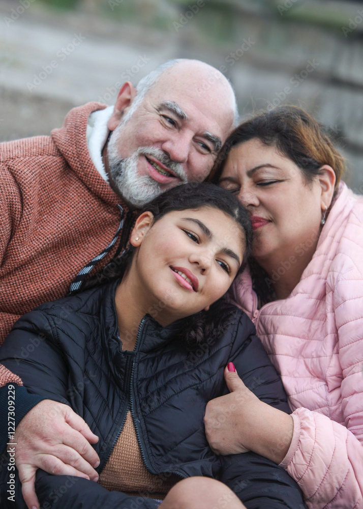 portrait of happy latino family, mature couple with teenage girl, hugging outdoors sitting on stairs on cloudy cold day portrait of happy latino family, mature couple with teenage girl, hugging outdoors sitting on stairs on cloudy cold day